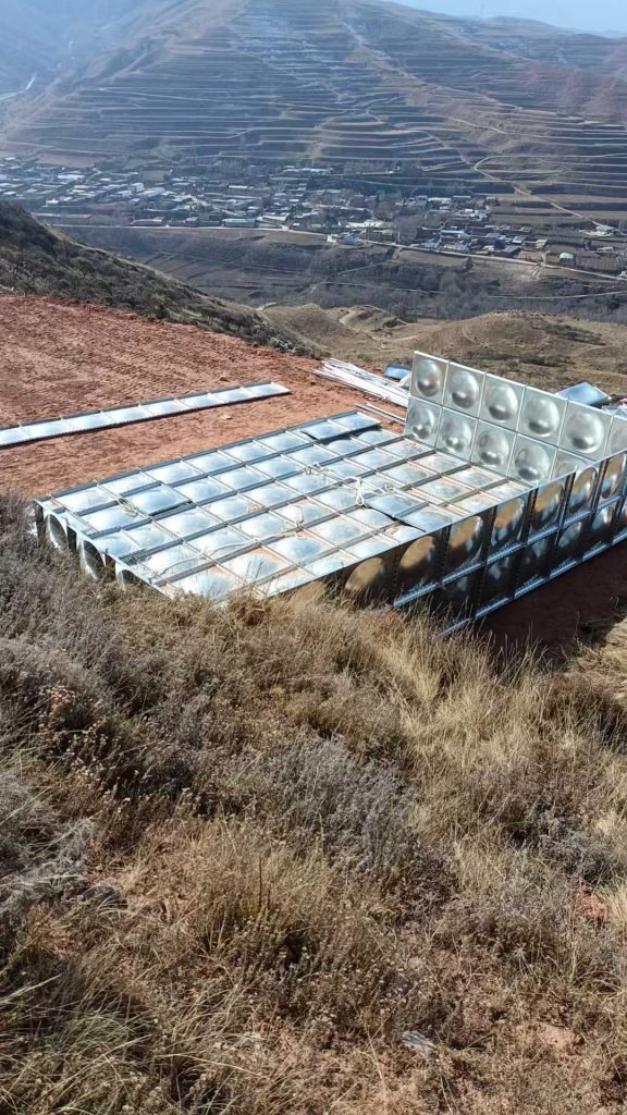 Large modular steel water storage tank installed on uneven plateau terrain for farming and livestock water management.