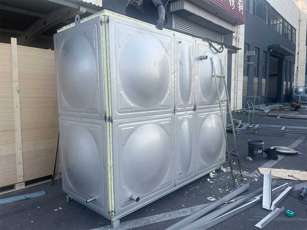 Workers are installing the insulation layer on a stainless steel water tank.